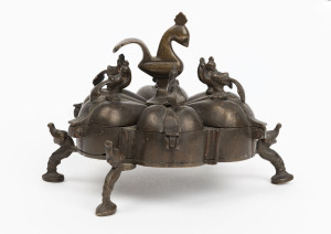 An Indian cast and patinated table storage box in the form of a lotus flower with peacock finials, the larger peacock finial locking the 6 lidded compartments, early 20th century, 9cm high, 14cm diameter