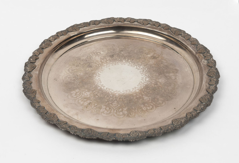 A vintage silver plated serving platter, with a decorative grape and vine leaf border and central pressed scroll engraving. Marked to the underside edge 'Carrington, reproduction, old Sheffield Plate', 40.5cm diameter,