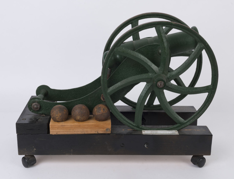 A miniature cast iron cannon on later wooden cradle with three unassociated display cannon balls, early to mid 20th century, bearing plaque "Brought From Liverpool To Australia In 1946 By Jacob A. Booth", 33cm high, 56cm long