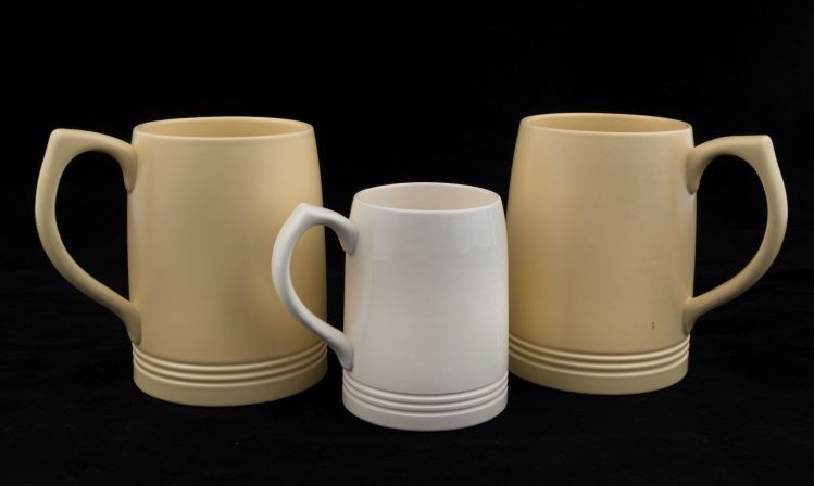 KEITH MURRAY: Three Wedgwood cream and yellow porcelain tankards. The two yellow examples with signature stamps "Keith Murray Wedgwood, Made In England", the other stamped "Wedgwood Of Etruria & Barlaston, Made In England, K.M.", the tallest 12cm high