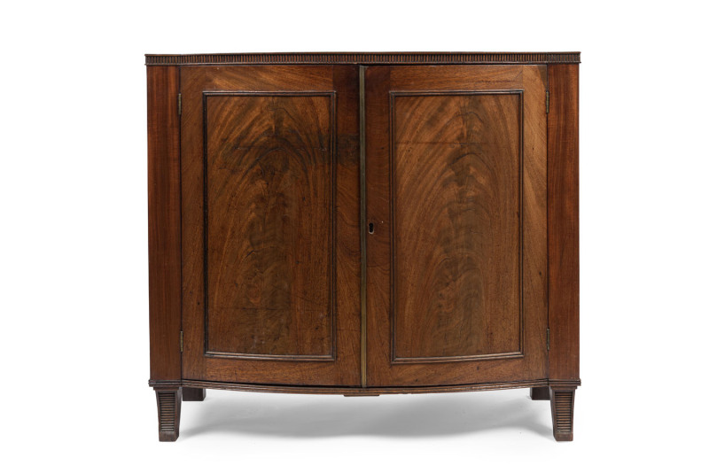 A Georgian bow front two door cabinet with book-matched flame mahogany panels, brass reeded trim and unusual vertical fluted edge, circa 1800, 86cm high, 97cm wide, 54cm deep