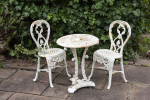 A three piece antique cast iron garden setting comprising two chairs and circular table, the table 61cm high, 50cm diameter