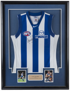GLEN ARCHER - NORTH MELBOURNE: signature on North Melbourne guernsey, captioned with two inset images of Archer in action, window mounted, framed and glazed; overall 102x79cm.
