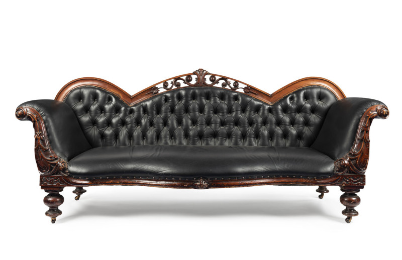 A Colonial double ended settee with serpentine front and pierced carved back, Australian cedar with diamond button black leather upholstery, Melbourne origin, circa 1865, 90cm high, 226cm wide, 75cm deep