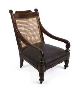 An antique Colonial library reading chair, Australian cedar with scrolling arm supports and turned front legs, upholstered in brown leather with hand caned back, Tasmanian, origin, circa 1840s, 97cm high, 61cm across the arms