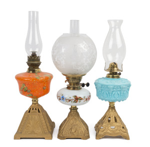 Three kerosene lamps each with gilt painted cast metal bases, one depicting King Edward VII, the other two with Art Nouveau cast decoration, each with coloured glass fonts, one with painted floral design, one pastel blue glass with moulded flowers, the th