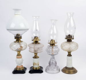 Four kerosene lamps, two with coloured glass columns, another with pressed white and peach glass stand on ebonised cast metal base, the fourth with clear pressed glass stand with impressed floral design and reeded font, all with brass burners and clear gl