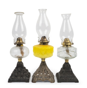 Three kerosene lamps with cast iron bases, each with pressed glass fonts, one canary yellow with flower decoration, the other two of clear pressed glass, each with single brass burner and glass chimneys, early 20th century, (3 items), the largest 51cm hig