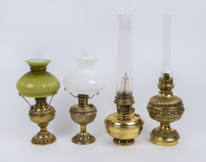 Four pressed and spun brass kerosene lamps, three with floral, reeded and fluted decoration, the fourth of plain squat form, each with brass burners and glass chimneys, two with coloured glass shades, early 20th century, (4 items), the taller 50cm high