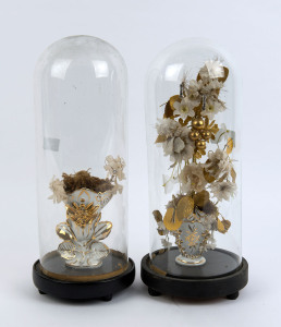 A pair of cylindrical French glass domes, both housing a gilt decorated Continental vase with faux flower display, standing on a ebonised timber plinth bases with three bun feet. 19th and 20th century. Dome measurements 36cm high, 13.5cm diameter.