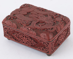A Chinese cinnabar lacquer box, early 20th century Decorated to the hinged lid with a scrolling dragon, and floral motifs to the sides. Cinnabar on cast brass ground with internal blue enamel finish. 5.5cm high, 11cm wide, 8cm deep.