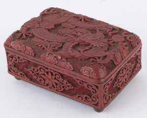 A Chinese cinnabar lacquer box, early 20th century Decorated to the hinged lid with a scrolling dragon, and floral motifs to the sides. Cinnabar on cast brass ground with internal blue enamel finish. 5.5cm high, 11cm wide, 8cm deep.