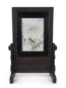 WANG YOUTANG (active 1890-1907), Chinese porcelain table screen in carved wooden stand. The panel decorated with mountain landscape and poem with artist square cartouche in iron red, late Qing Dynasty, 78cm high, 51cm wide, 24cm deep. Note: Illustrated i