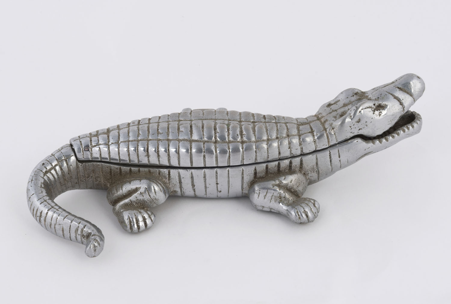 An antique cigarette box in the form of a crocodile, cast metal with chrome  finish, early 20th century, with internal compartments labelled Cigarettes  and Matches with striking pad, 24cm long