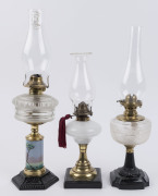 Three kerosene lamps on black painted cast iron bases, brass single burners and clear glass chimneys, early 20th century, (3 items), the largest 55cm high