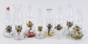 A collection of eight early 20th century portable kerosene lamps, each with moulded and pressed clear glass fonts of various forms and decoration with carrying handle, brass single wick burners fitted to each, all with clear glass chimneys, (8 items), the