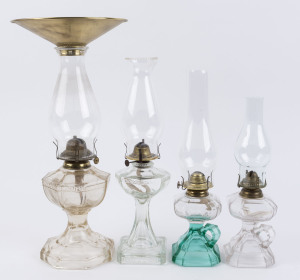 Four pressed glass kerosene table lamps, two with Greek key pattern border to the faceted octagonal fonts on column stands with stepped bases, the smaller two in clear and two tone clear and green glass with carrying handles, each with single brass burner