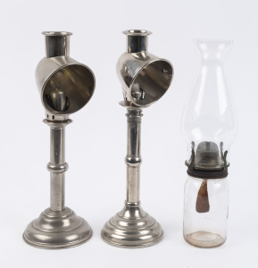Two nickel plated candlestick lamps with fitted chimney hoods, each with spring loaded candle feeder mechanism on ring turned stands and moulded bases, along with a simple pressed glass jar kerosene lamp with single burner and glass chimney, early 20th ce