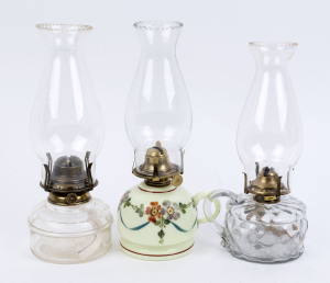 Three glass kerosene lamps, one with green opaque glass base with hand painted decoration and carrying handle, the other two with clear pressed glass bases, one with carrying handle, all with single wick brass burners and clear glass chimneys, (3 items), 