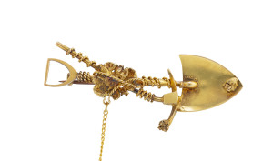 An 18ct gold miner's brooch, crossed pick and shovel with entwined rope and nugget specimen, 19th century, stamped "18ct", ​5.5cm wide, 5 grams