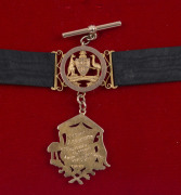 15ct gold fob (approx. 6gms) suspended from a black silk band enhanced with an additional fob featuring a 9ct gold Coat of Arms of Australia, two gold shields and gold fittings. The fob engraved verso "CORP J.C. DOGGETT 107 HOWITZER BATTERY, AUST. FIELD A - 2