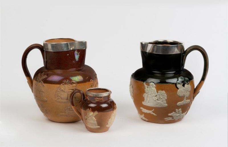 DOULTON LAMBETH group of three pottery jugs with sterling silver mounts, early 20th century, impressed marks to the bases, ​the largest 16cm high