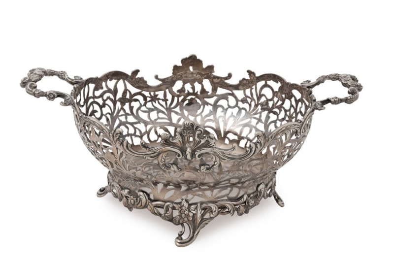 An antique English sterling silver fruit basket. Particularly well crafted in pierced silver of oval form with two shaped floral work handles and scrolling Rococo revival feet. Made by William Comyns of London, circa 1904, 15cm high, 38cm wide, 1212 grams