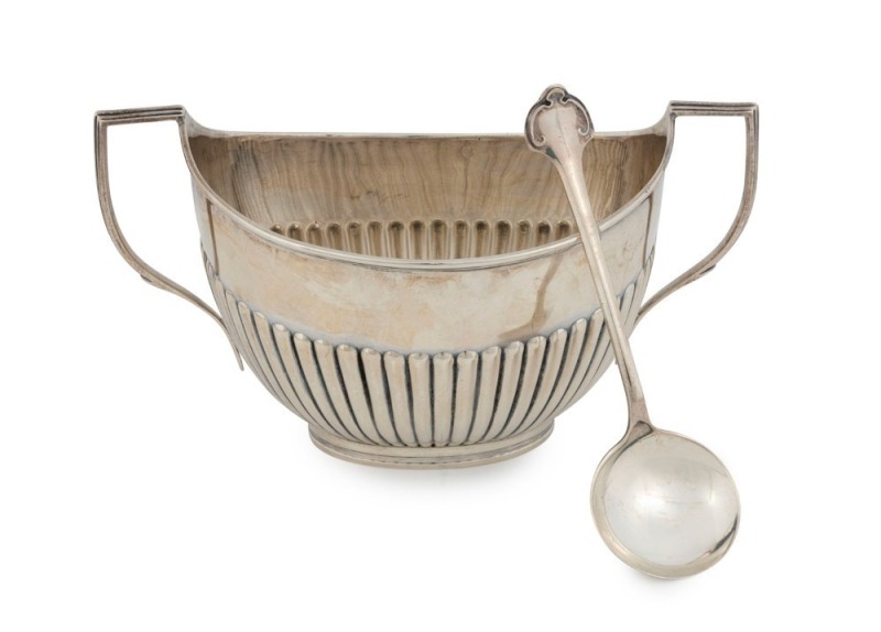An Edwardian sterling silver two handled boat shaped sugar basin in the classical style. Raised reeded sides to the lower body with an oval inset raised foot base and two attractive tapering and reeded geometric loop handles. Made by W. Hutton & Sons Limi