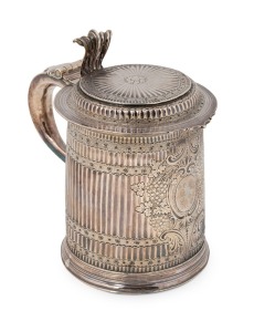 A Queen Anne sterling silver covered tankard of early design, made by John Gibbons of London, circa 1702, Circular reed and flute decorated raised plinth base with vertically fluted sides and bands of wriggle work. Stamped floral motif and a large engraving cartouche with armorial engraved crest to centre front flanked by embossed fruiting vine leaves. Hinged flat cover with raised platform to the centre part and a central floral design with radiating flute decoration.