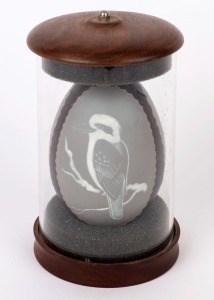 A carved emu egg depicting an Aborigine, Emu & Kookaburra in separate panels, housed in acrylic display case, circa 1980, 19cm high