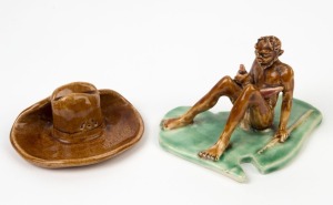 Australian pottery statue of an Aboriginal seated figure on Australian map base, together with a slouch hat ornament, (2 items), the map base 13cm high