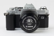 Canon AL-1 QF SLR camera, 1982 [#1097585] with Canon FD 50mm f1.8 lens [#5980840], the commemorative lens cap "OFFICIAL 35MM CAMERA * 1984 OLYMPIC GAMES". - 2