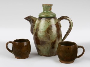 A green glazed pottery teapot and two cups, (3 items), incised "L.M.", the teapot 21cm high