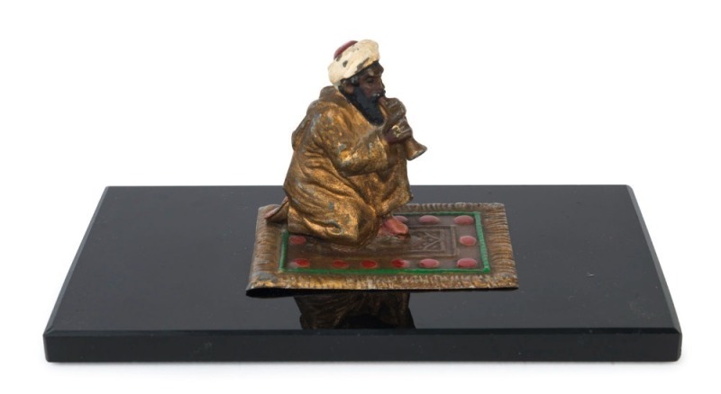 An Austrian cold painted bronze statue of an Arab sitting on a Persian carpet, mounted on a black glass plinth, early 20th century, ​​​​​​​6cm high, 13.5cm wide, 7cm deep