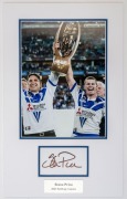 CANTERBURY-BANKSTOWN: small mounted display featuring photo Steve Price holding Premiership Cup aloft following their 2004 Grand Final win, SIGNED BY PRICE on piece beneath, overall 44x27cm, with CofA.