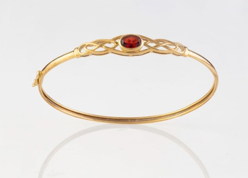 A 9ct yellow gold bangle with a red garnet, 20th century, ​​​​​​​6.5cm wide, 4.6 grams