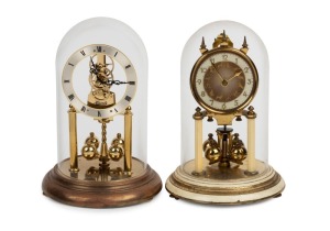 Two German 400 day anniversary clocks in glass domes, one with skeleton dial the other with cream enamel decoration, 20th century, 22cm and ​​​​​​​23cm high each overall