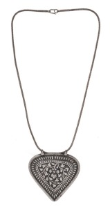 An antique Malay silver modesty disc (caping) of heart shape. The main decorative border is embedded with a row of padi seeds followed by a row of embossed dots inside a thin border. The central shield adorned with floral decoration. With original silver chain (50 cm long). Terengganu, Northeast Malaysia, circa 1900. Private collection, Melbourne. Acquired in Singapore in 1980. 7cm high, 6.5cm wide, 31 grams. Note: The last known cases of babies wearing the caping was during the reign of Sultan