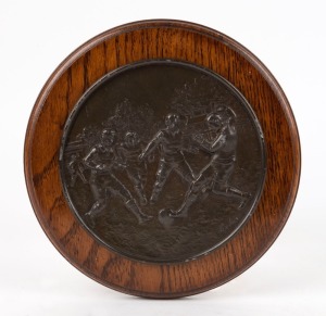 "The Football Tackle" French cast and patinated spelter wall plaque on oak backboard, signed "Calier", circa 1940. 22cm diameter.