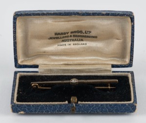 An Art Deco bar brooch with solitaire white diamond mounted in platinum set in yellow gold, housed in a HARDY BROS. Ltd. plush box, circa 1925, 5.3cm wide, 2.9 grams
