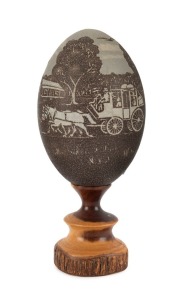 A carved emu egg ornament with stagecoach in farm landscape, mounted on a mulga wood plinth, paper label reads "This Emu shell carving is mounted on MULGA. By K. WARD, Bourke. Licence No. G.L.89", ​​​​​​​20cm high