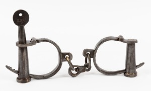A pair of antique style metal handcuffs with key, late 20th century, 29cm wide