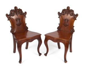 A fine pair of Australian cedar hall chairs with Rococo scroll carved back rests and applied central shield, the curved and reeded front chair rail terminating with accentuated cabriole legs, N.S.W. origin, circa 1860. 92cm high, 48cm wide