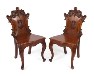 A fine pair of Australian cedar hall chairs with Rococo scroll carved back rests and applied central shield, the curved and reeded front chair rail terminating with accentuated cabriole legs, N.S.W. origin, circa 1860. 92cm high, 48cm wide