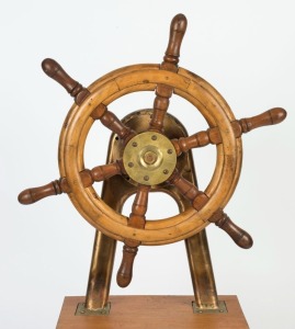 A ship's wheel and brass mount on later timber stand, early 20th century, the wheel 60cm wide, 141cm high overall