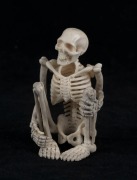 A carved antler statue of a squatting skeleton figure, 20th century, 8cm high 