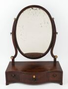 A Georgian mahogany oval toilet mirror with serpentine front, barber pole string inlay and whale bone roundels, late 18th century, 57cm high, 43cm wide, 21cm deep 