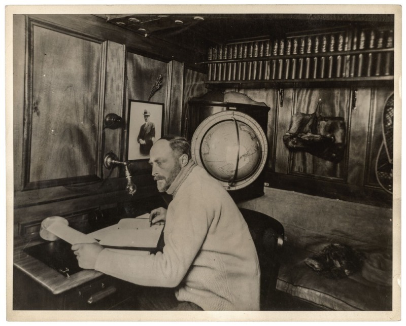 THE B.A.N.Z. ANTARCTIC EXPEDITION: Official original photograph by Captain Frank Hurley: Image A29 - Title: Sir Douglas Mawson...in his study aboard The Discovery. with official "MAWSON ANTARCTIC EXPEDITION" handstamp and release date "TUESDAY APR. 15, 19