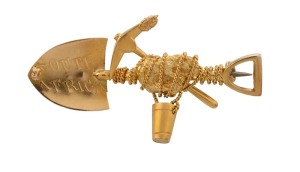 A South African 18ct miner's brooch with crossed pick and shovel, designed with gold nugget specimen and bucket entwined in rope, stamped "18 L.P., South Africa", 4.7cm wide, 6.5 grams