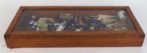 A glass-top display case with various items including vintage fans, an ambrotype in case, badges, vintage eye-glasses, etc. 30 x 78 x 9cm.